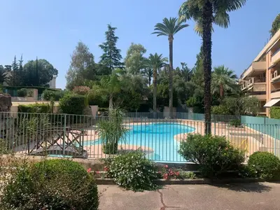 a swimming pool with a fence and palm trees at Appt 2ch 90m2 avec terrasse 40m2, piscine et tennis in Cannes