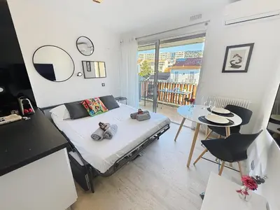 a bedroom with a bed and a table and a room with a balcony at Bright and vast studio terrace easy parking Cannes heart of town 1 mn in Cannes