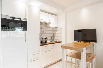 a kitchen with white cabinets and a table and a tv at Renovated apt with Parking & Terrace - Palm Beach in Cannes