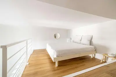a white bedroom with a white bed and wooden floors at LE PETIT PALAIS avec mezzanine de charme au cœur de Cannes in Cannes