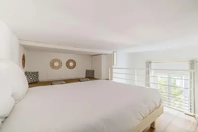 a white bedroom with a large white bed and a window at LE PETIT PALAIS avec mezzanine de charme au cœur de Cannes in Cannes