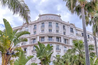 a large white building with palm trees in front of it at Croisette 65 apartment-Miramar residence in Cannes