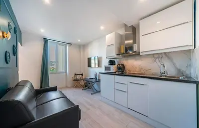 a kitchen with white cabinets and a black leather couch at Close to train station and palace, quiet in Cannes