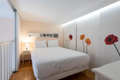 a bedroom with a white bed with red flowers on it at LE RIMBAUD splendide duplex dans le Suquet, près des plages et du Palais des Festivals in Cannes