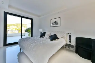 a white bedroom with a large bed and a chair at L'HORIZON avec somptueuse terrasse vue mer in Cannes