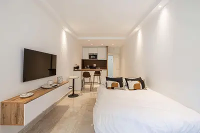 a bedroom with a large white bed and a kitchen at LE CENTER avec joli balcon et parking pour un plaisant séjour in Cannes