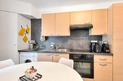 a kitchen with wooden cabinets and a white table at LE PALME D'OR splendide studio cocon près de la Croisette, du Palais et des plages in Cannes