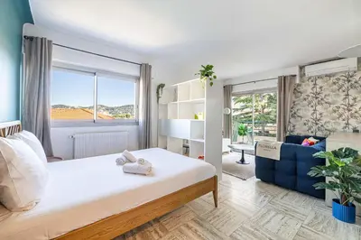 a bedroom with a large bed and a blue couch at LA PALMERAIE joyeux studio avec balcon, à deux pas de la Banane in Cannes