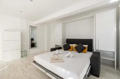 a white bedroom with a large bed with a sign on it at LE LOUIS BLANC avec balcon en plein centre-ville in Cannes