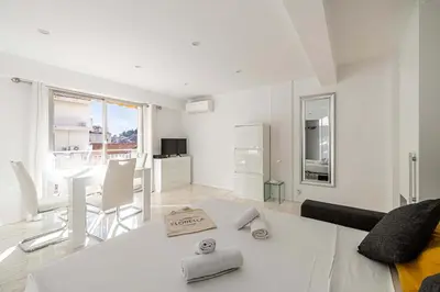 a white living room with a table and a kitchen at LE LOUIS BLANC avec balcon en plein centre-ville in Cannes