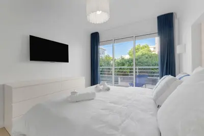a white bedroom with a large white bed with a flat screen tv at 2 chambres - Grand balcon - à 1 min de la plage in Cannes