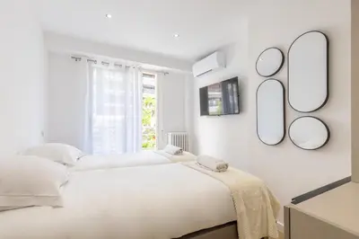 a white bedroom with two beds and mirrors on the wall at LB Vacation Rentals I Beautiful 2BR Apt, Renovated in 2025, La Croisette, Minutes from Beach and Palais in Cannes