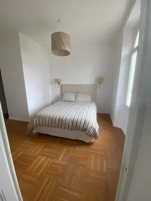 a bed in a white room with a wooden floor at Lisa Appartement de charme in Cannes