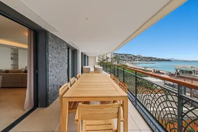 a balcony with a wooden table and chairs and the ocean at REF 1998 - Cannes - Sea view apartment for rent in Cannes