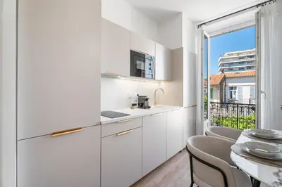 a kitchen with white cabinets and a table with chairs at Appartement Caire - Welkeys in Cannes