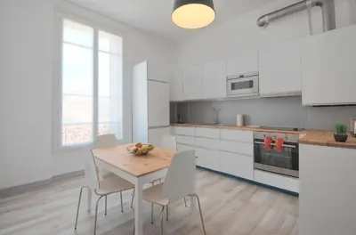 a white kitchen with a wooden table and chairs at Residence Michel Ange in Cannes