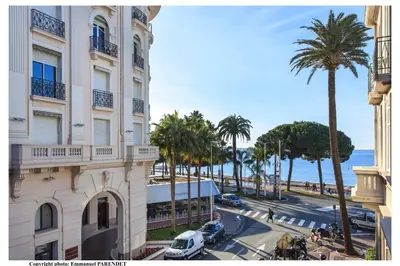 a building and a street with palm trees and the ocean at REF 961 - Cannes Croisette - Sea view apartment for rent in Cannes
