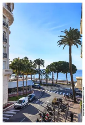 a street with palm trees and a street with cars and motorcycles at REF 961 - Cannes Croisette - Sea view apartment for rent in Cannes