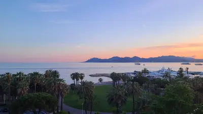 a view of the ocean and palm trees at sunset at Vue unique sur toute la baie de Cannes et la mer in Cannes