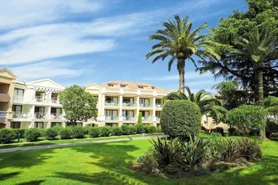 a large white building with palm trees and a lawn at Vue Mer, Piscine de ouf Votre Oasis à Cannes in Cannes
