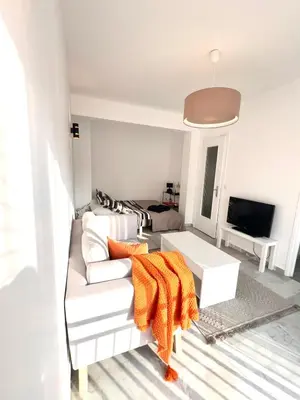 a living room with a white couch with an orange blanket at studio luxueux in Le Cannet