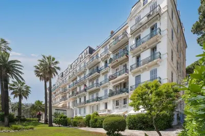 a large white building with palm trees at Appartement Beau Site - Welkeys in Cannes