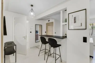a kitchen with black bar stools and white walls at Modern 2 chambres - Jardin - rue du Martinez in Cannes