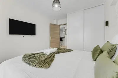 a white bedroom with a bed with a tv on the wall at Modern 2 chambres - Jardin - rue du Martinez in Cannes
