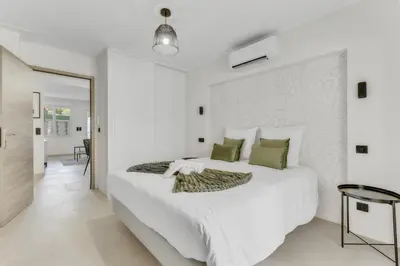 a white bedroom with a large white bed with green pillows at Modern 2 chambres - Jardin - rue du Martinez in Cannes