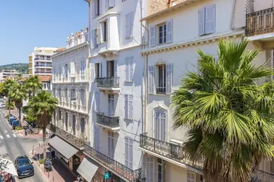 a tall white building with a palm tree next to a street at Apartment 2 bedrooms near beach - Cannes in Cannes