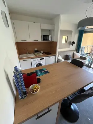 a kitchen and living room with a wooden table at Le Beach 1 min plage , piscine , terrasse in Cannes
