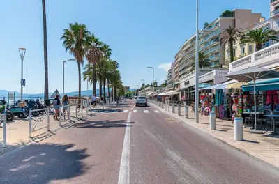 a street with palm trees and people walking down the street at Le 45 Clémenceau - Superbe logement proche plages et Palais in Cannes