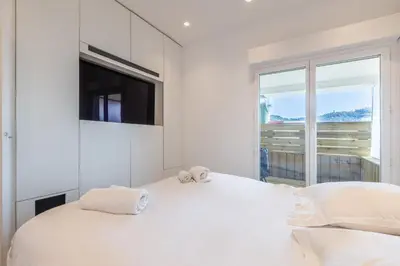 a white bedroom with a large bed and a flat screen tv at LB Vacation Rentals I Elegant Apartment with Terrace & Mezzanine in the heart of Cannes in Cannes