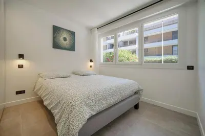 a white bedroom with a bed and two windows at Modern 3BR with Patio, Walk to Beach and Croisette in Cannes