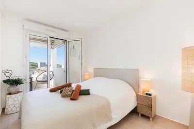 a bedroom with a white bed and a balcony at Appartement Grand Balcon Sud avec Piscine proche Cannes in Le Cannet