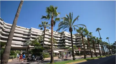 a large white building with palm trees on a street at Gray D'albion Cannes centre , 1 min des plages in Cannes