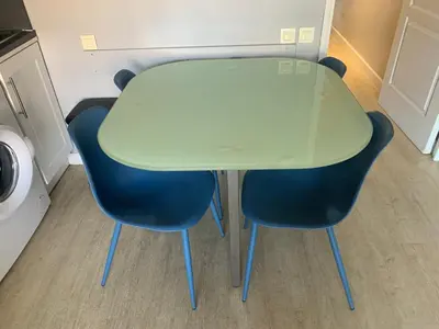 a glass table and two blue chairs in a room at 2 pièces vue piscine et plage à 2min in Cannes