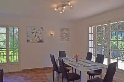 a dining room with a table and chairs and windows at Villa Super Cannes avec vue mer in Vallauris