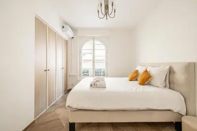 a white bedroom with a large bed with a chandelier at LE PASTEUR pour tout confort en plein cœur de Cannes in Cannes