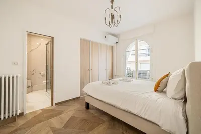 a white bedroom with a large bed and a chandelier at LE PASTEUR pour tout confort en plein cœur de Cannes in Cannes