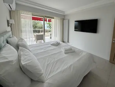 a white bedroom with a large white bed and a television at Elegant 2 Br with parking in Cannes