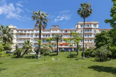 a large building with palm trees in a park at LB Vacation Rentals I Luxurious 1BR with parking & terrace in Cannes