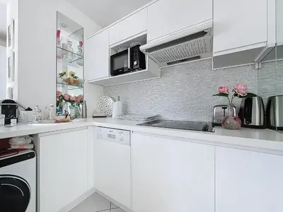a white kitchen with white cabinets and pink roses at INTUITION Studio avec terrasse 3min Croisette in Cannes
