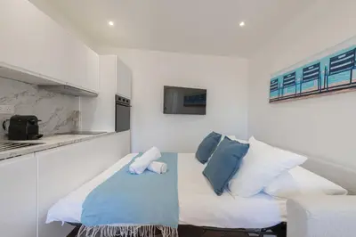 a small white kitchen with a bed with blue pillows at Cannes 1-Br Apartment Near the City Center in Cannes