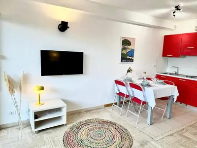 a living room with a table and a kitchen with red cabinets at Le 65 Picaud - Superbe logement proche plages in Cannes