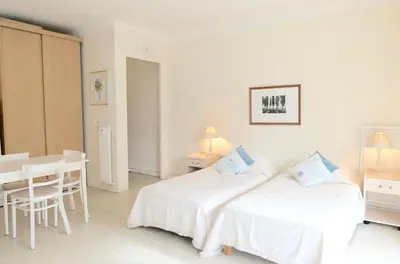 two beds in a white room with a table and a desk at Spacious Studio Apartment Near The Beach - 2313 in Cannes