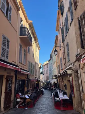 a street with people sitting at tables in an alley at La petite MAISON BLANCHE CANNES in Cannes
