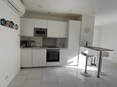a kitchen with white cabinets and a table with a chair at La petite MAISON BLANCHE CANNES in Cannes