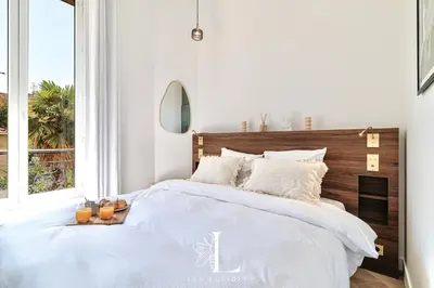 a white bedroom with a large bed with a wooden headboard at Les Lucioles 5- Luxury 2-Bedroom Apartment in Cannes