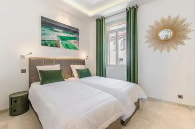 two beds in a bedroom with green curtains and a mirror at Cozystay 1243 Port & Sea View Cannes in Cannes